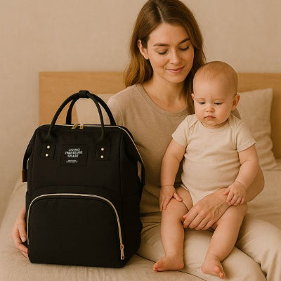 Sac a langer noir maman assise a cote avec bebe sur les pied 